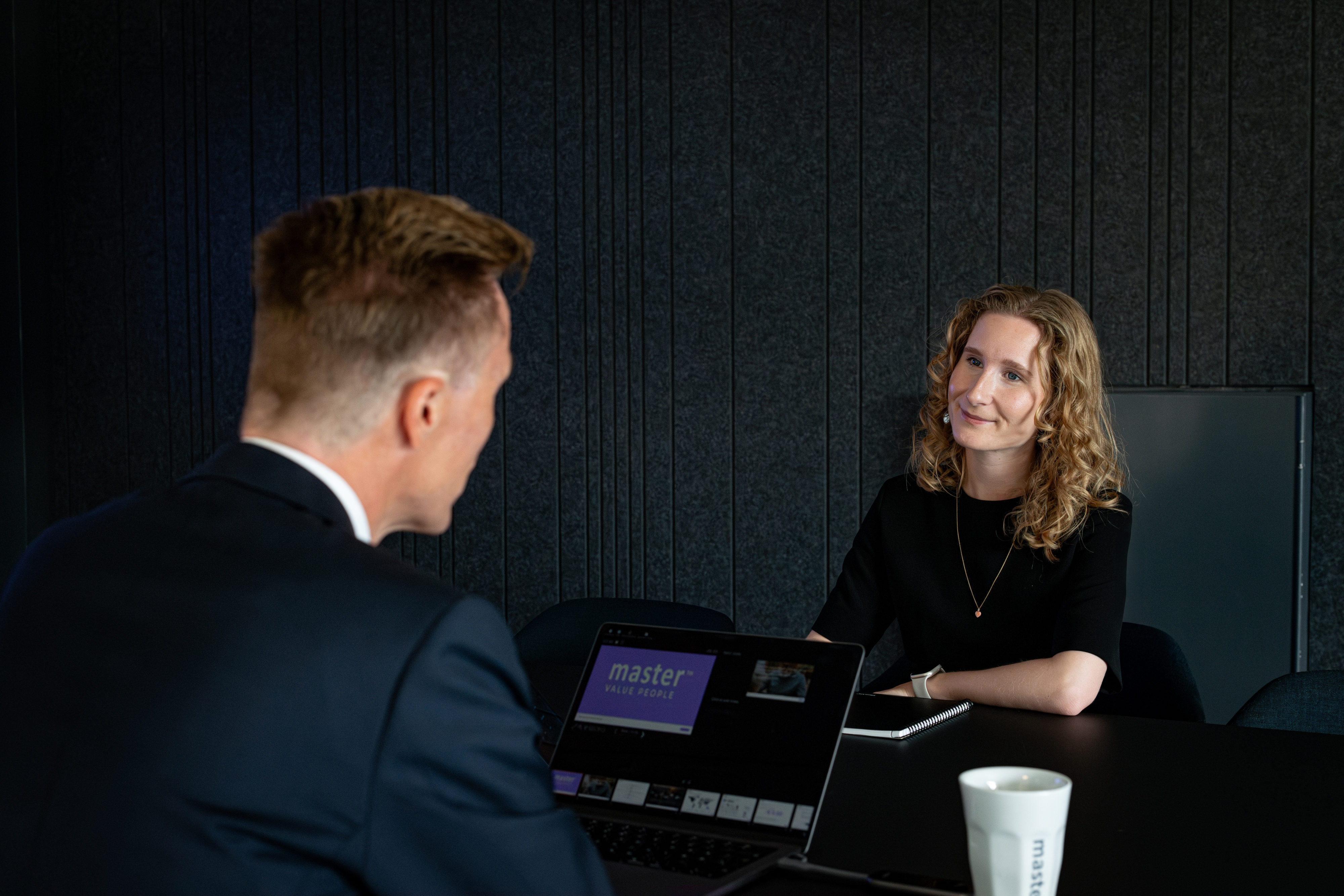 mand i jakkesæt med ryggen til kameraet taler med en ung kvinde med lyst krøllet hår om Master Danmarks testværktøjer